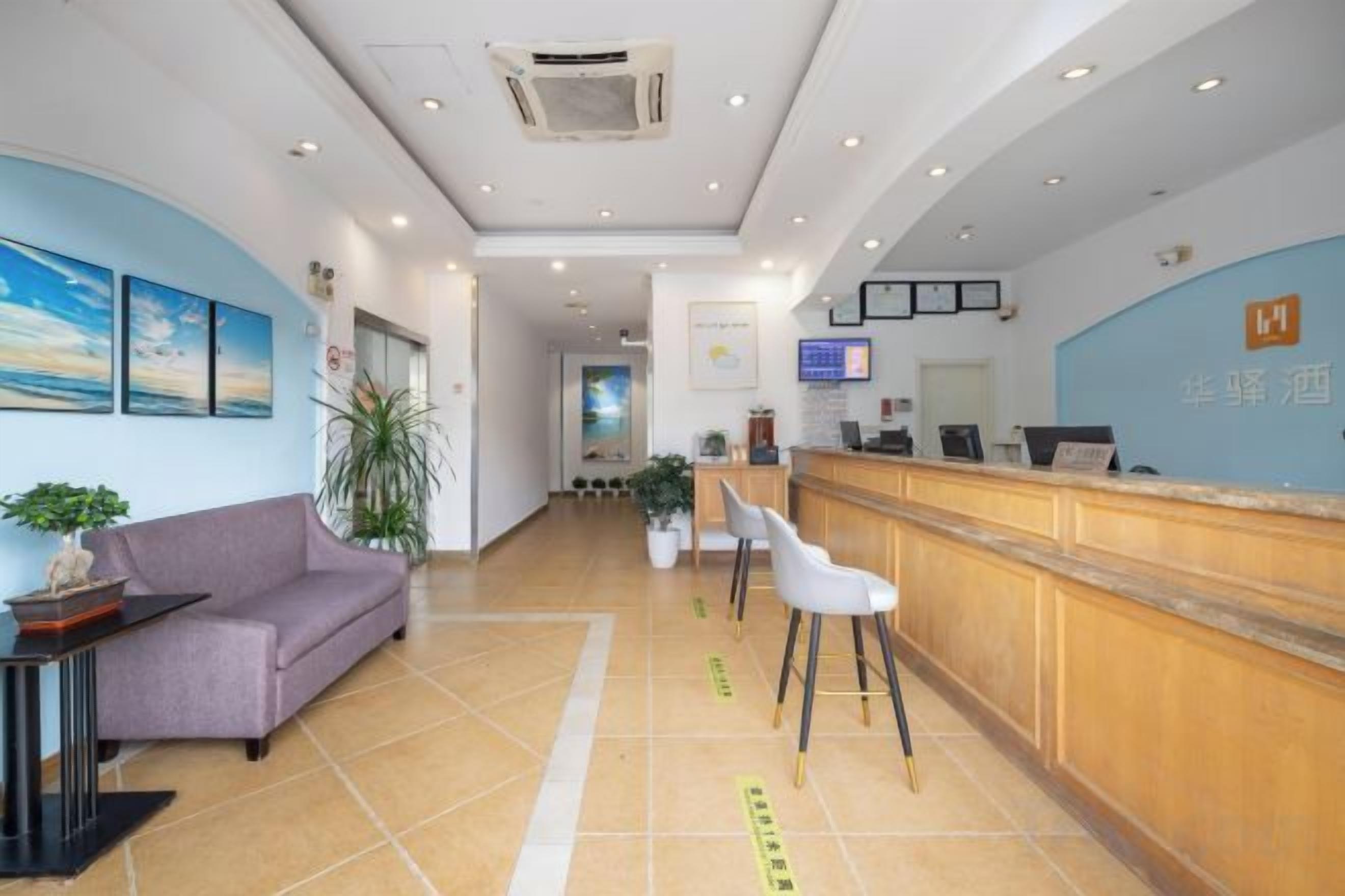A hotel reception area with a reception desk, a sofa, chairs, and a potted plant.