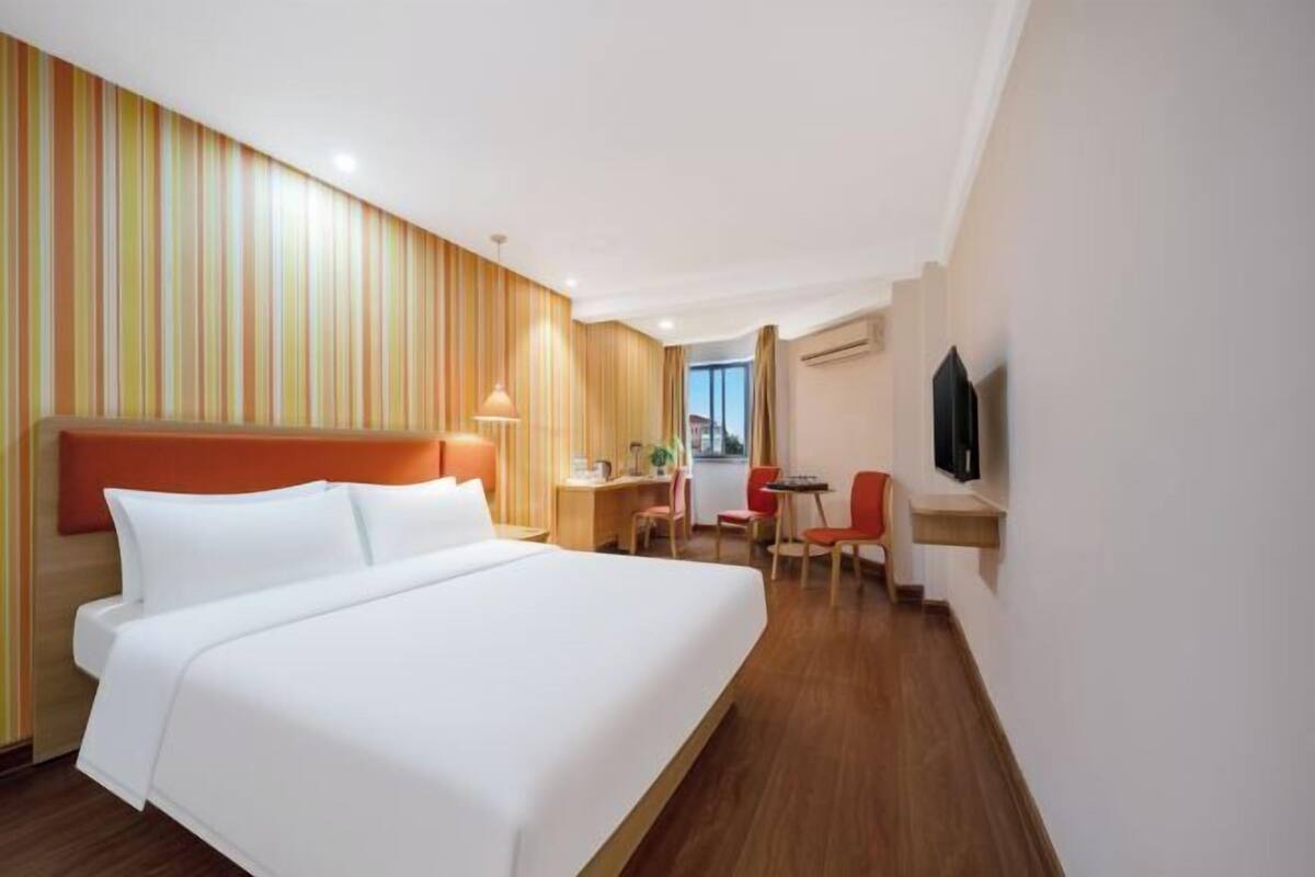 A hotel room with a large bed, a desk, two chairs, a television, and a window.