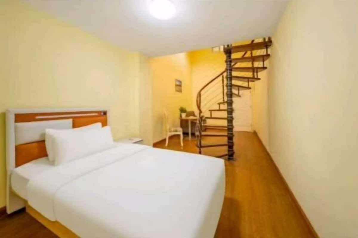 A hotel room with a wooden bed, a white headboard, and a spiral staircase leading to an upper level.