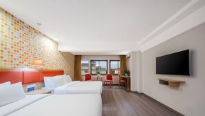 Ein Hotelzimmer mit zwei Betten, einem Schreibtisch, einem Stuhl, einem Fernseher und einem Fenster mit Vorhängen.