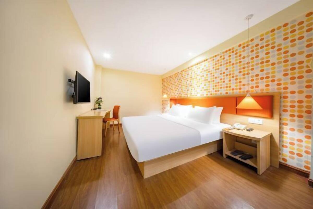 A hotel room with a bed, bedside table, lamp, and a TV mounted on the wall.