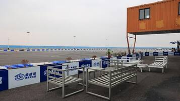 An outdoor seating area with metal tables and chairs, a building with a window, and a blue and white fence.