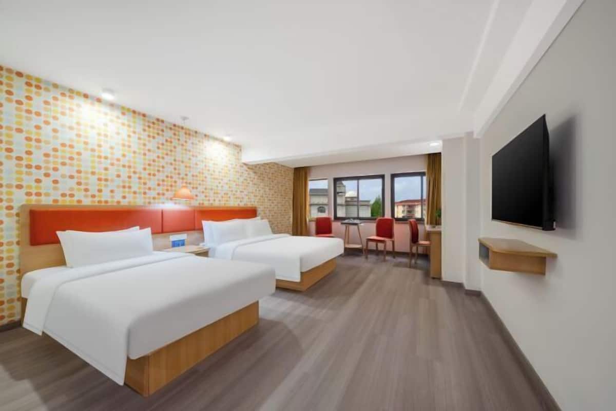 A hotel room with two beds, a TV, a desk, and a window with a view.