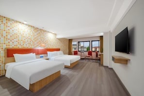 A hotel room with two beds, a TV, a desk, and a window with a view.