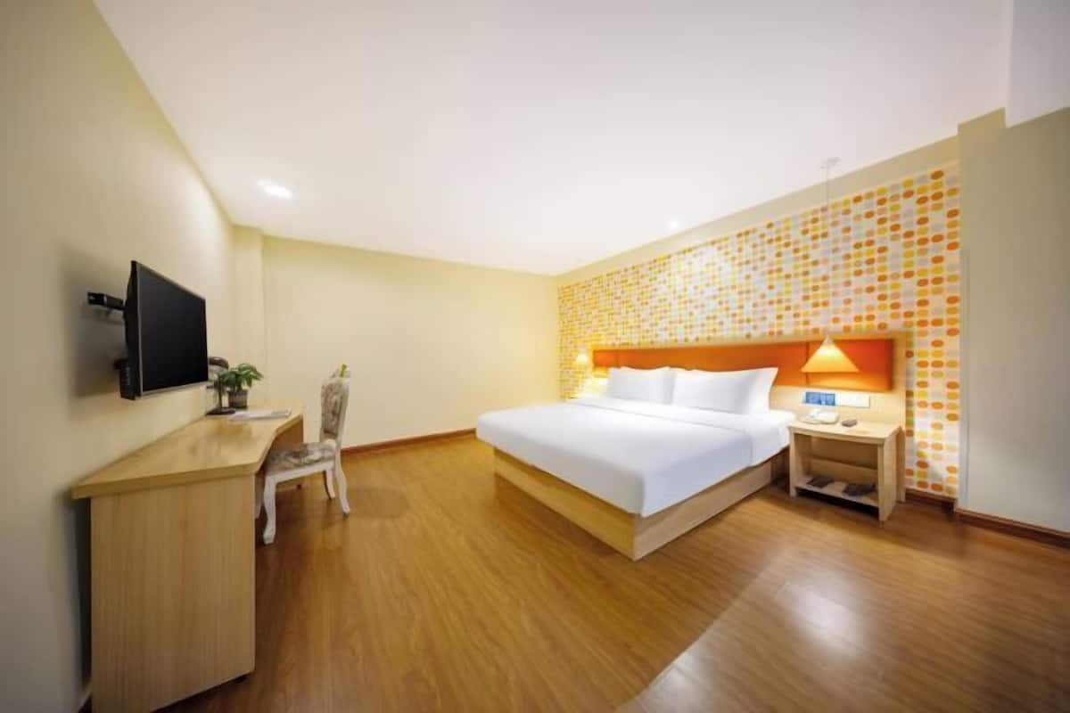A hotel room with a bed, a desk, a chair, a TV, and a wall with a patterned design.