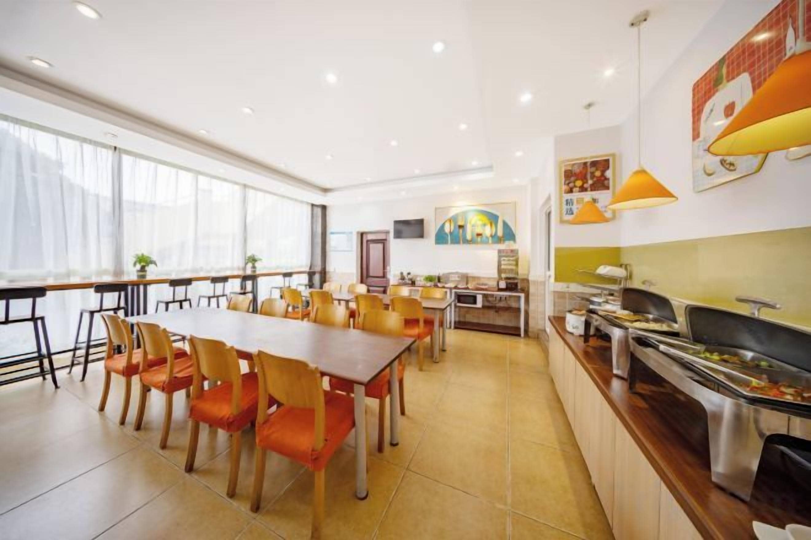 A dining area with a long table and chairs, a buffet counter, and a kitchen area.