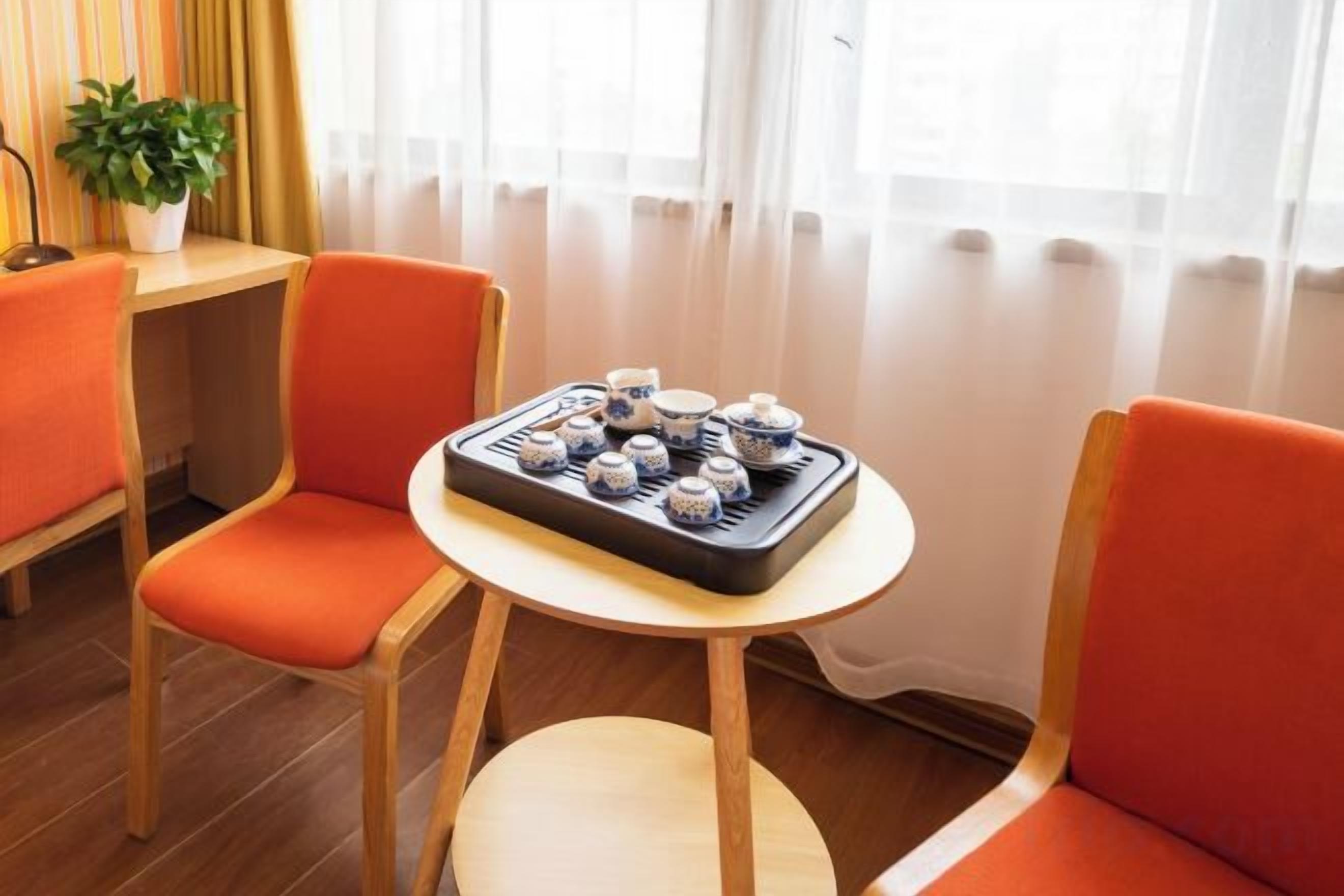A room with two orange chairs, a small round table with a tray of teapots, and a potted plant.