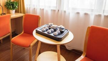 A room with two orange chairs, a small round table with a tray of teapots, and a potted plant.