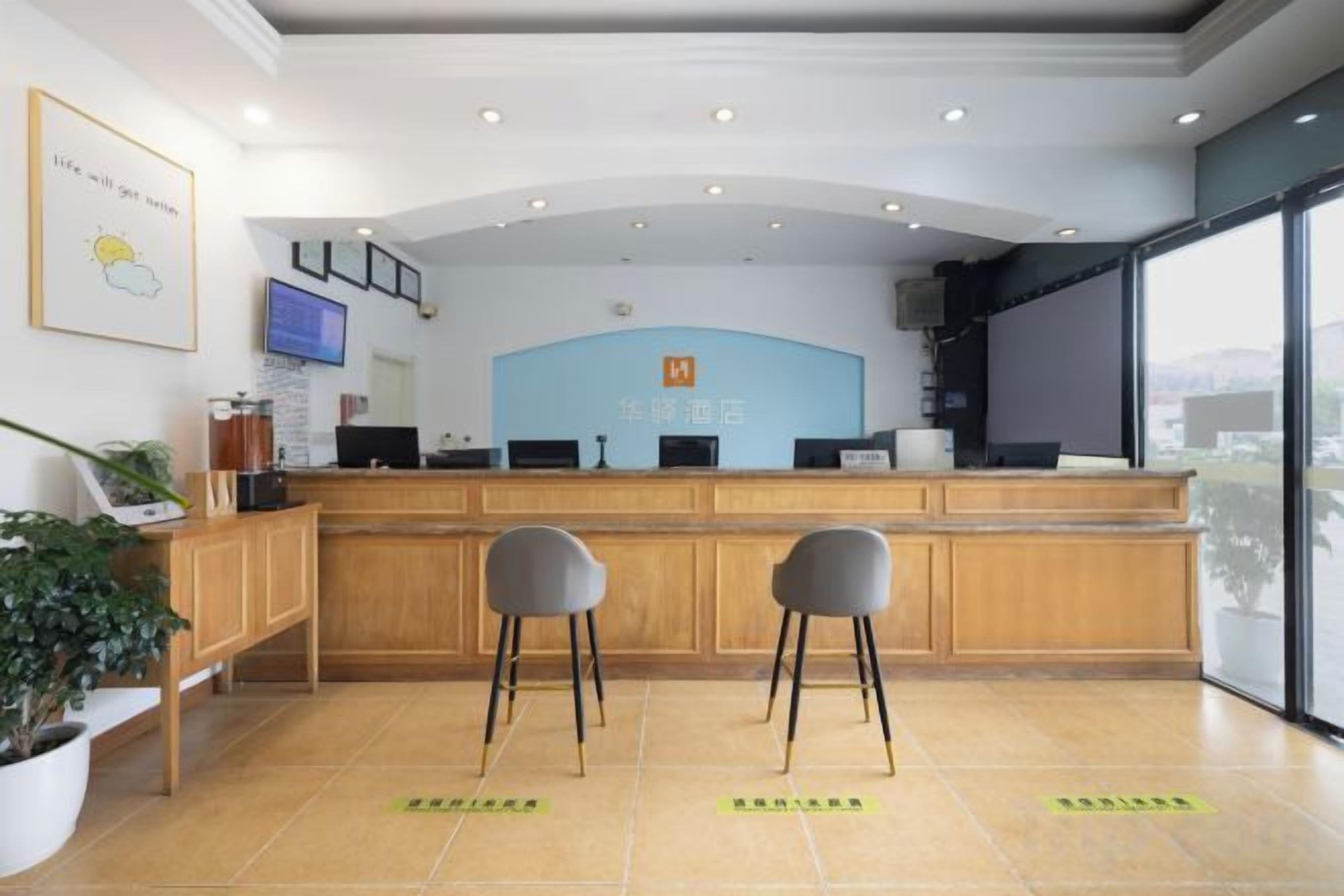 Un área de recepción con un mostrador de madera, dos taburetes de bar, un televisor y un ventanal grande.