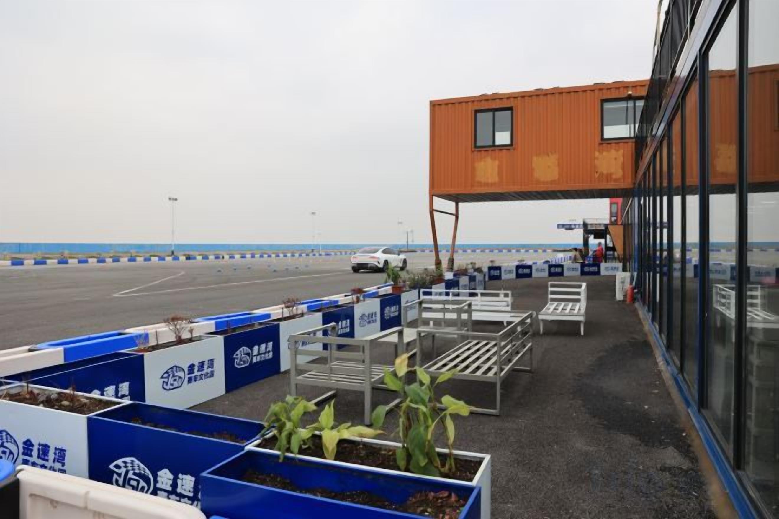 A parking area with blue barriers, a white car, and a building with large windows.