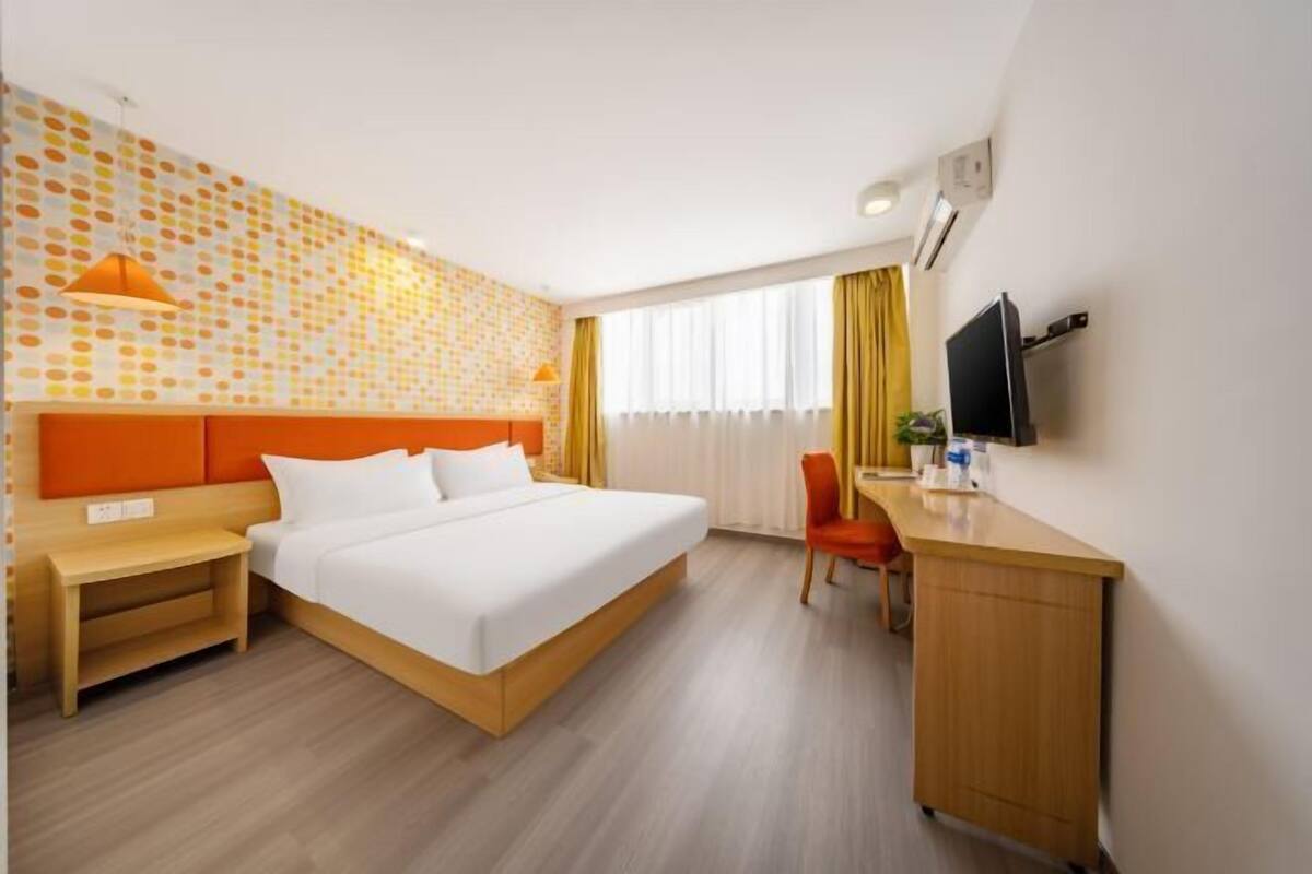 A hotel room with a large bed, a desk, a chair, a TV, and a wall with a polka dot pattern.