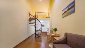 Ein Flur mit Holzboden, einer Wendeltreppe, einem grauen Sofa, einem kleinen runden Tisch und einem Gemälde an der Wand.