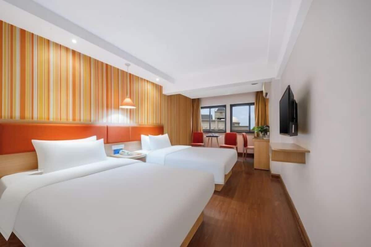 A hotel room with two beds, a TV, a desk, and a window with a view.