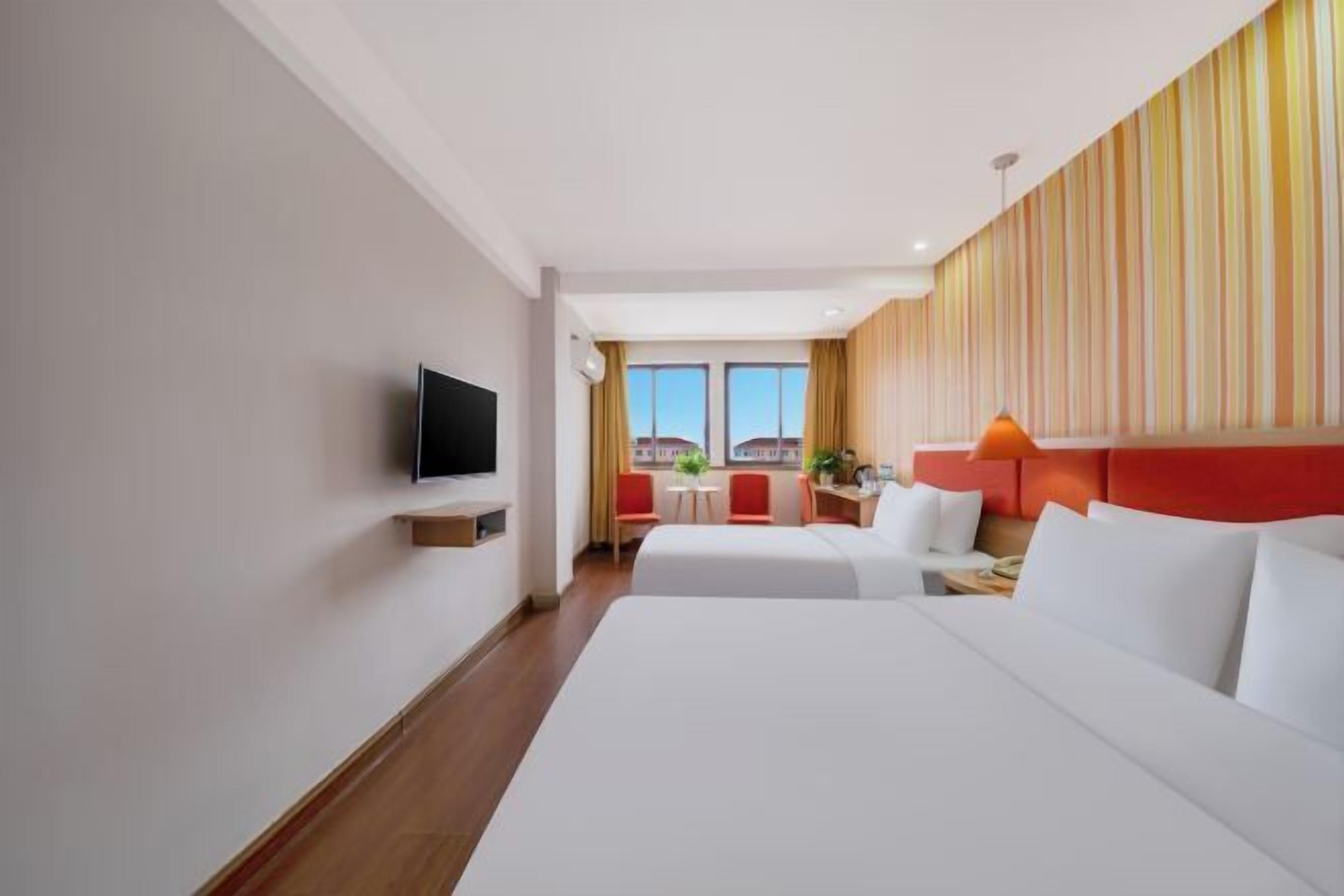Une chambre d’hôtel avec deux lits, une télévision, un bureau et une fenêtre avec des rideaux.