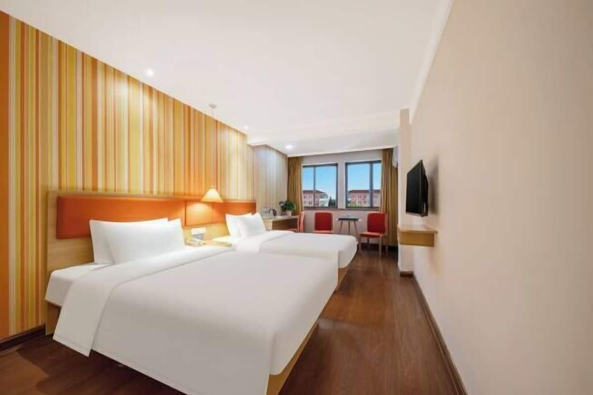 A hotel room with two beds, a TV, a desk, and a window with a view.
