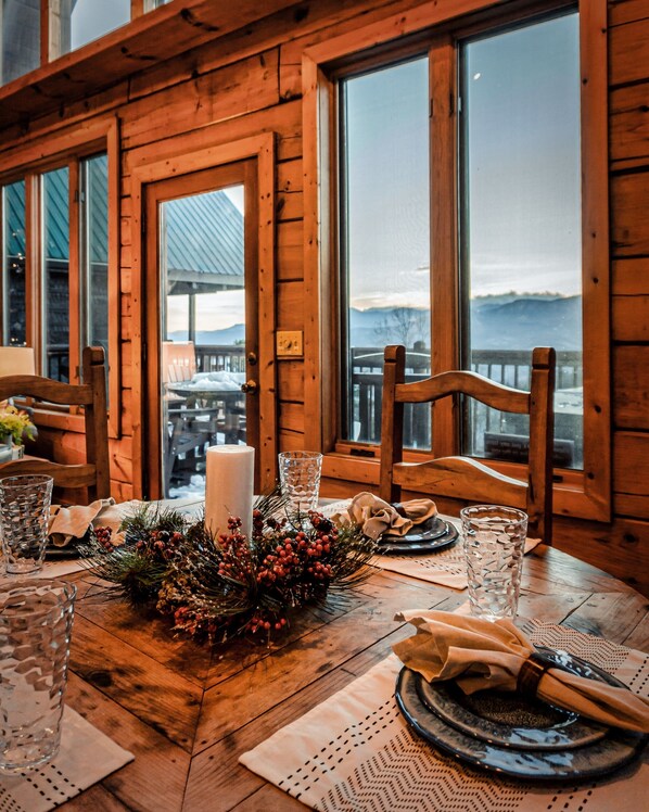 A wooden interior with a table set for dining, large windows, and a view of mountains.