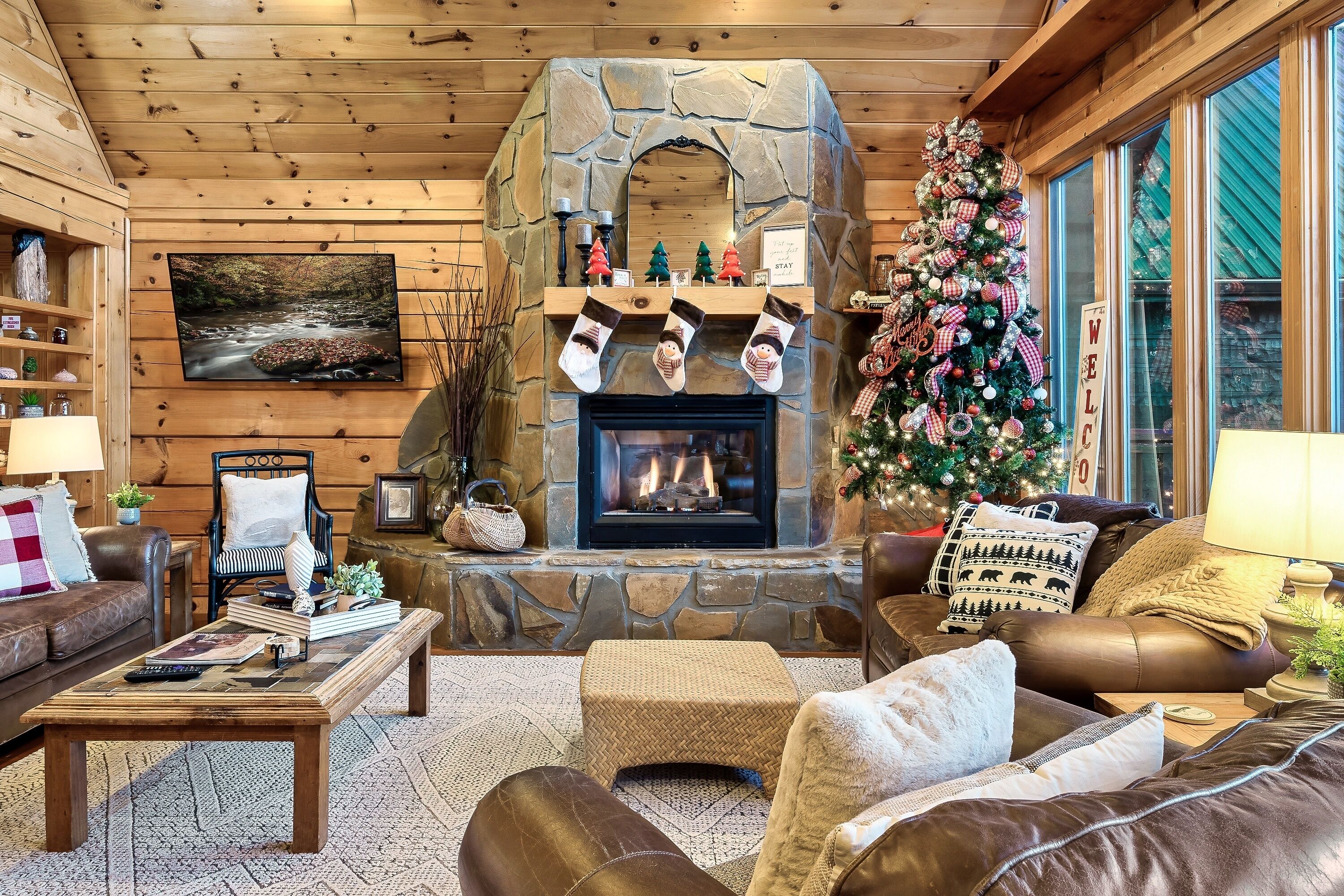 A cozy living room with a stone fireplace, leather sofas, a coffee table, and a Christmas tree.