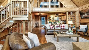 Un vaste espace de vie aménagé dans un style industriel, avec un plafond haut, des poutres en bois, un escalier, un grand canapé, une table basse et une table à manger.