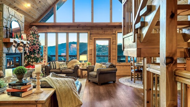 L’intérieur chaleureux d’un chalet en bois avec une cheminée, un sapin de Noël et une vue sur les montagnes.