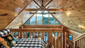 Une chambre confortable située sous les toits, avec un plafond en bois, une grande fenêtre et un lit recouvert d’une couverture à carreaux.