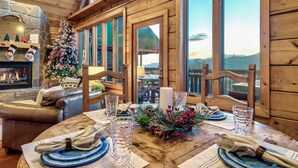L’intérieur chaleureux d’un chalet en bois, avec une table à manger dressée pour quatre personnes, un sapin de Noël et une cheminée.
