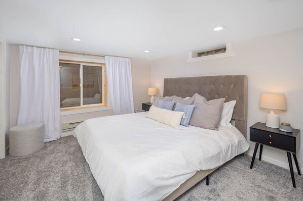 A bedroom with a large bed, a nightstand, a window with curtains, and a ceiling light. - Verbrick Street Vacation (Appleton)