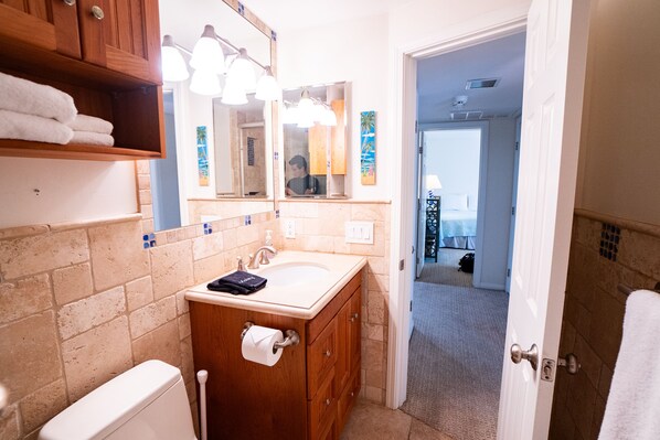 A bathroom with a wooden vanity, a sink, and a toilet. There is a towel rack with towels, a mirror, and a door leading to another room.