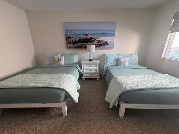 A bedroom with two beds, a nightstand, and a painting of a beach scene. - Mermaid’s Grotto - Beachfront 2BR on Carpinteria Sand (Carpinteria)