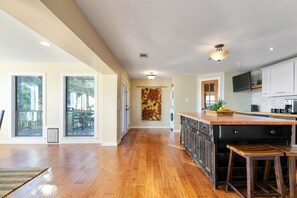 A spacious kitchen with a large island, wooden flooring, and a view of the outdoors through sliding glass doors.