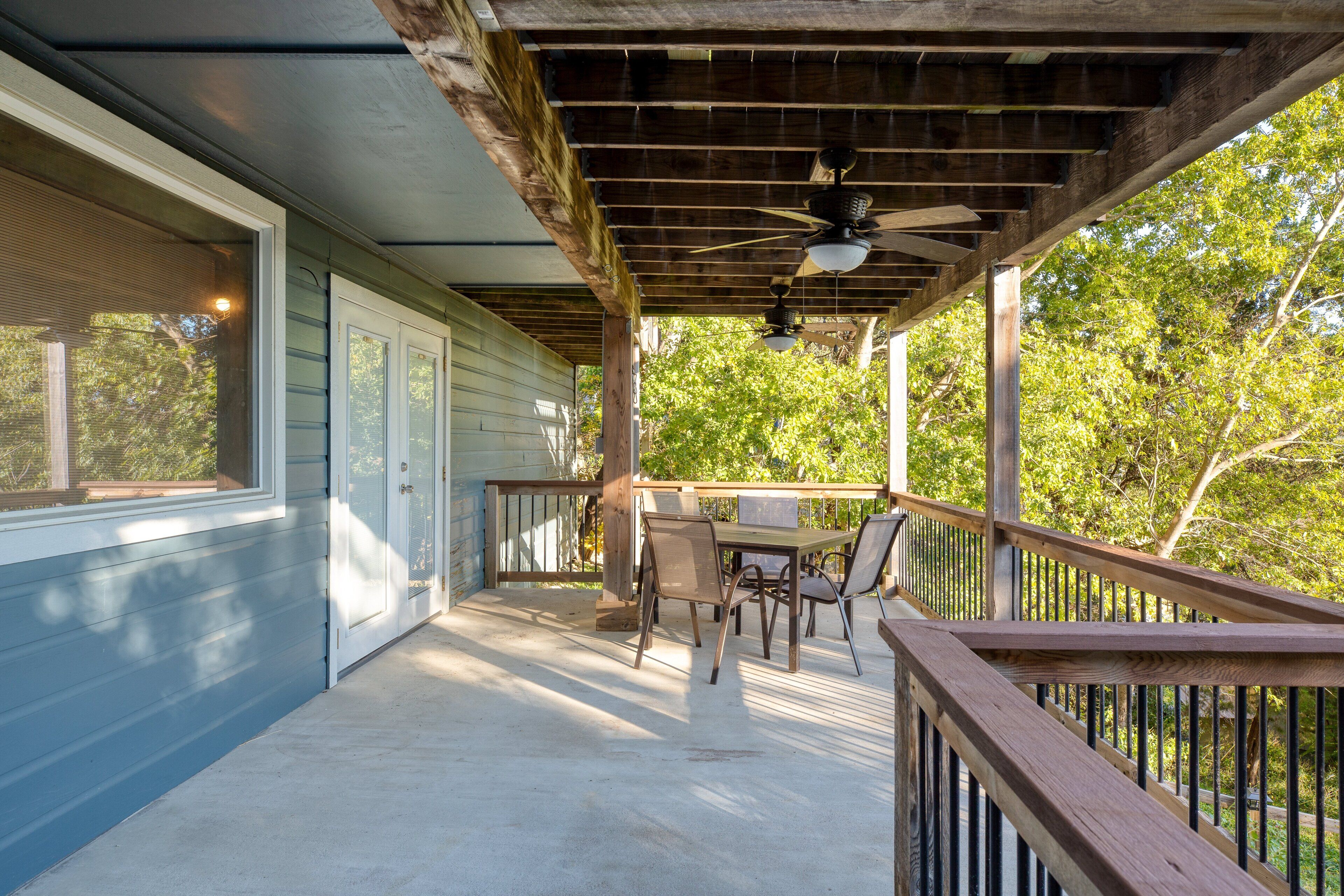 A covered porch with a ceiling fan, a table with chairs, and a view of trees.