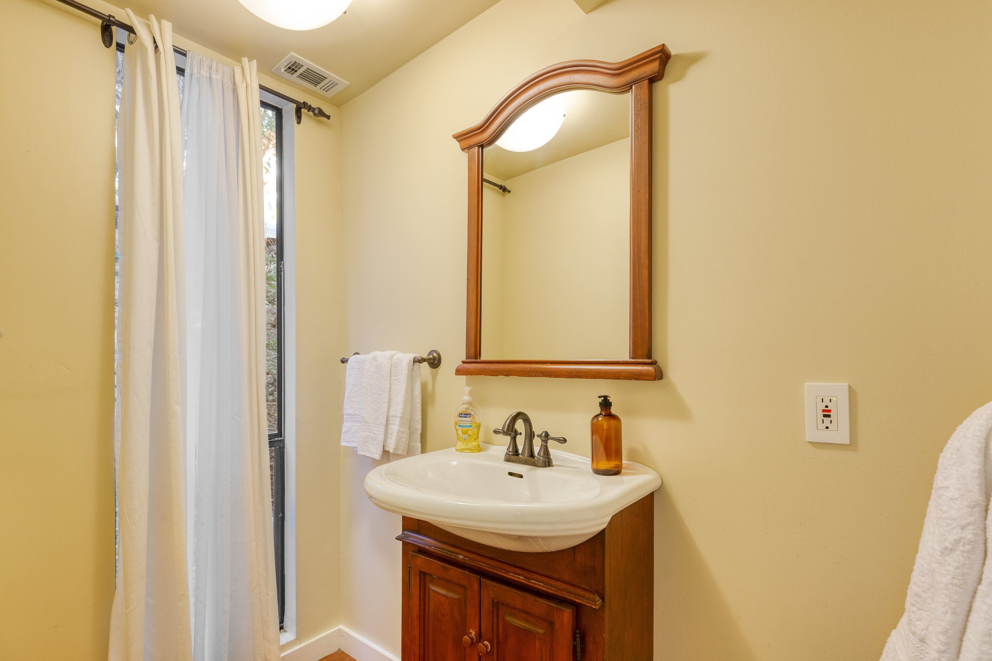 A bathroom with a white sink, wooden cabinet, and a mirror.