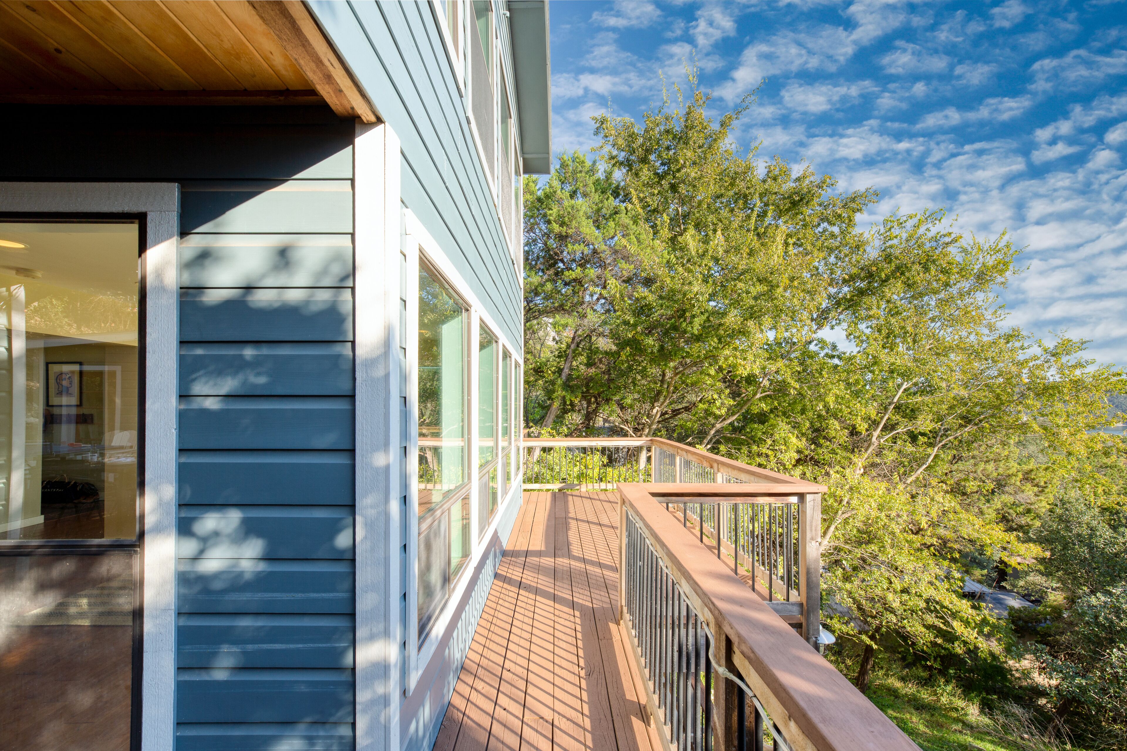 A wooden deck with a railing, overlooking a lush green landscape and a clear blue sky.