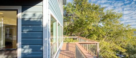 A wooden deck with a railing, overlooking a lush green landscape and a clear blue sky.