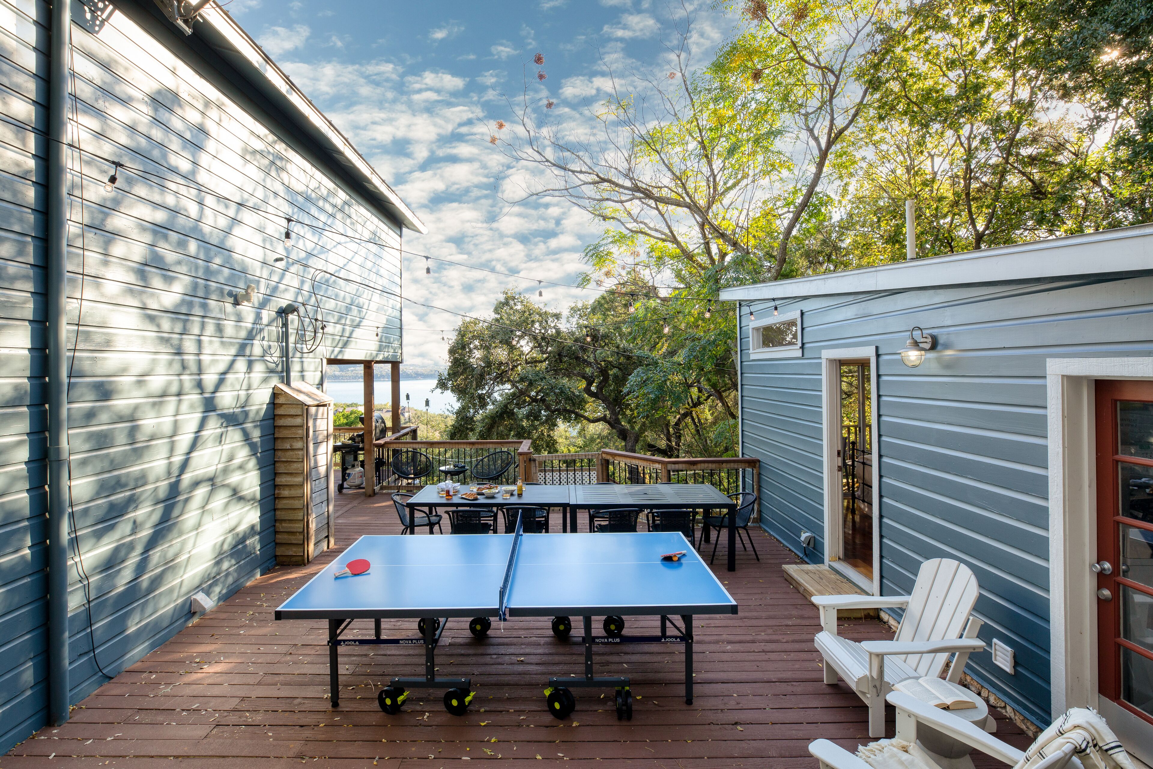 Une terrasse extérieure avec des tables de ping-pong, des chaises et un petit bâtiment doté d’une porte.