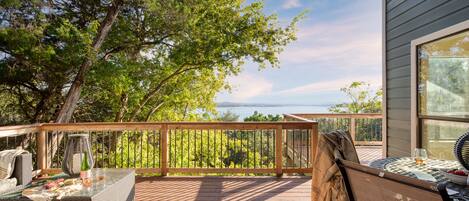 Um deck de madeira com móveis de exterior, uma mesa com tampo de vidro e vista para o oceano.