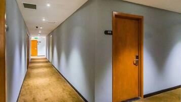 Un pasillo de hotel con suelo alfombrado, una puerta de madera y un interruptor de luz en la pared.