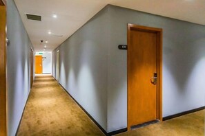 A hotel corridor with a carpeted floor, a wooden door, and a light switch on the wall. - 7 Days Premium (Shenzhen Bao'an Bus Station Haiya Mega Mall) (Shenzhen)