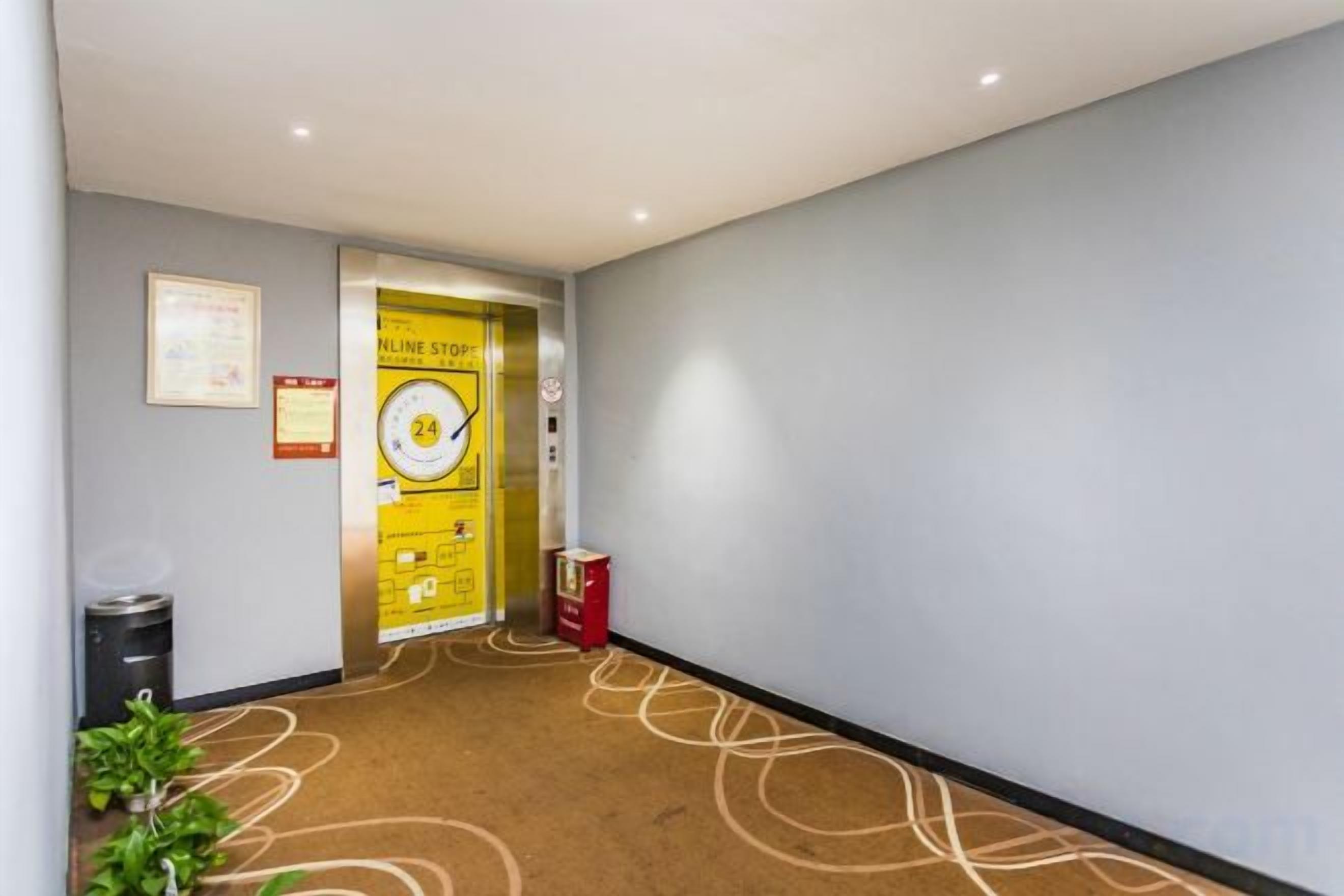A hotel corridor with a carpeted floor, a trash bin, a recycling bin, and a door with a sign.