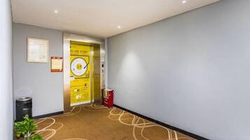 Pasillo de hotel con piso alfombrado, un bote de basura, un contenedor de reciclaje y una puerta con un cartel.
