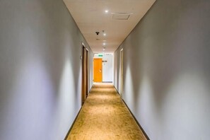 Um corredor comprido e estreito com piso coberto por carpete, portas em ambos os lados e teto com iluminação embutida.
