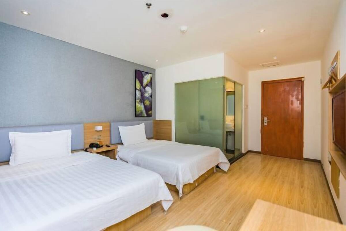 A hotel room with two beds, a wooden floor, a green wall, and a wooden door.