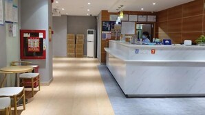 A hotel reception area with a marble counter, a small seating area with tables and chairs, and a refrigerator in the background. - 7 Days Premium (Shenzhen Bao'an Bus Station Haiya Mega Mall) (Shenzhen)