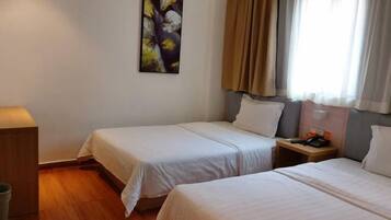 A hotel room with two beds, a nightstand with a phone and a lamp, a painting on the wall, and a window with curtains.