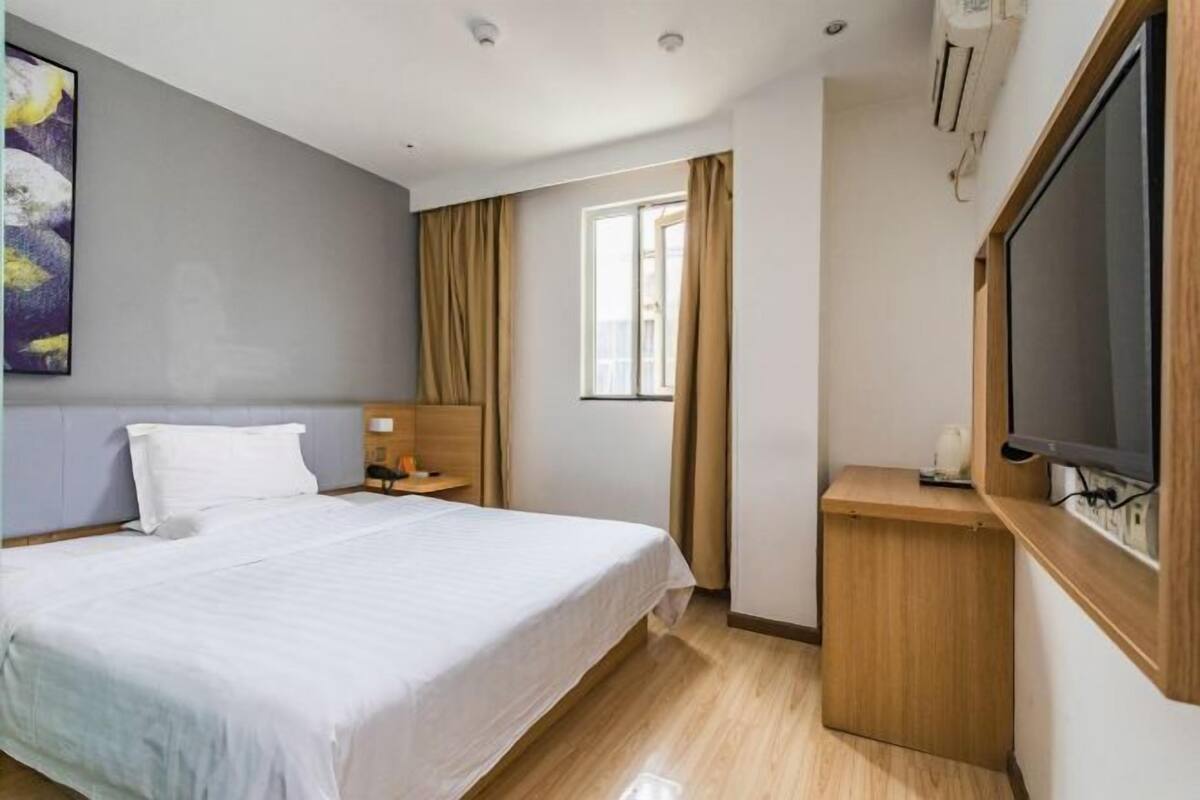 A hotel room with a bed, a TV, a desk, and a window with curtains.