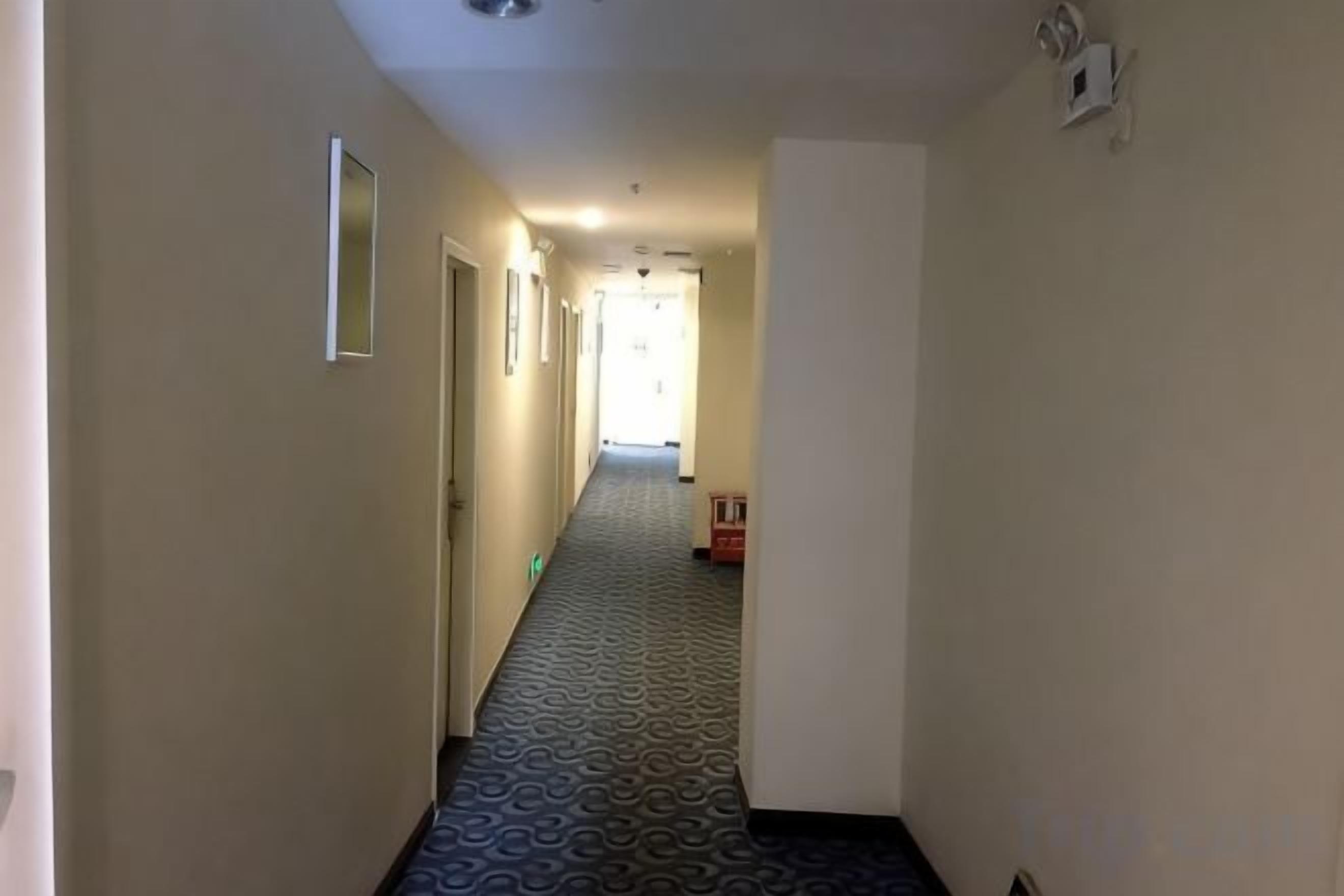A hotel hallway with patterned carpet, doors on both sides, and a fire alarm on the right wall.