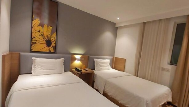 A hotel room with two single beds, a nightstand with a lamp, and a large floral artwork on the wall. - 7 Days Premium (Shenzhen Bao'an Bus Station Haiya Mega Mall) (Shenzhen)