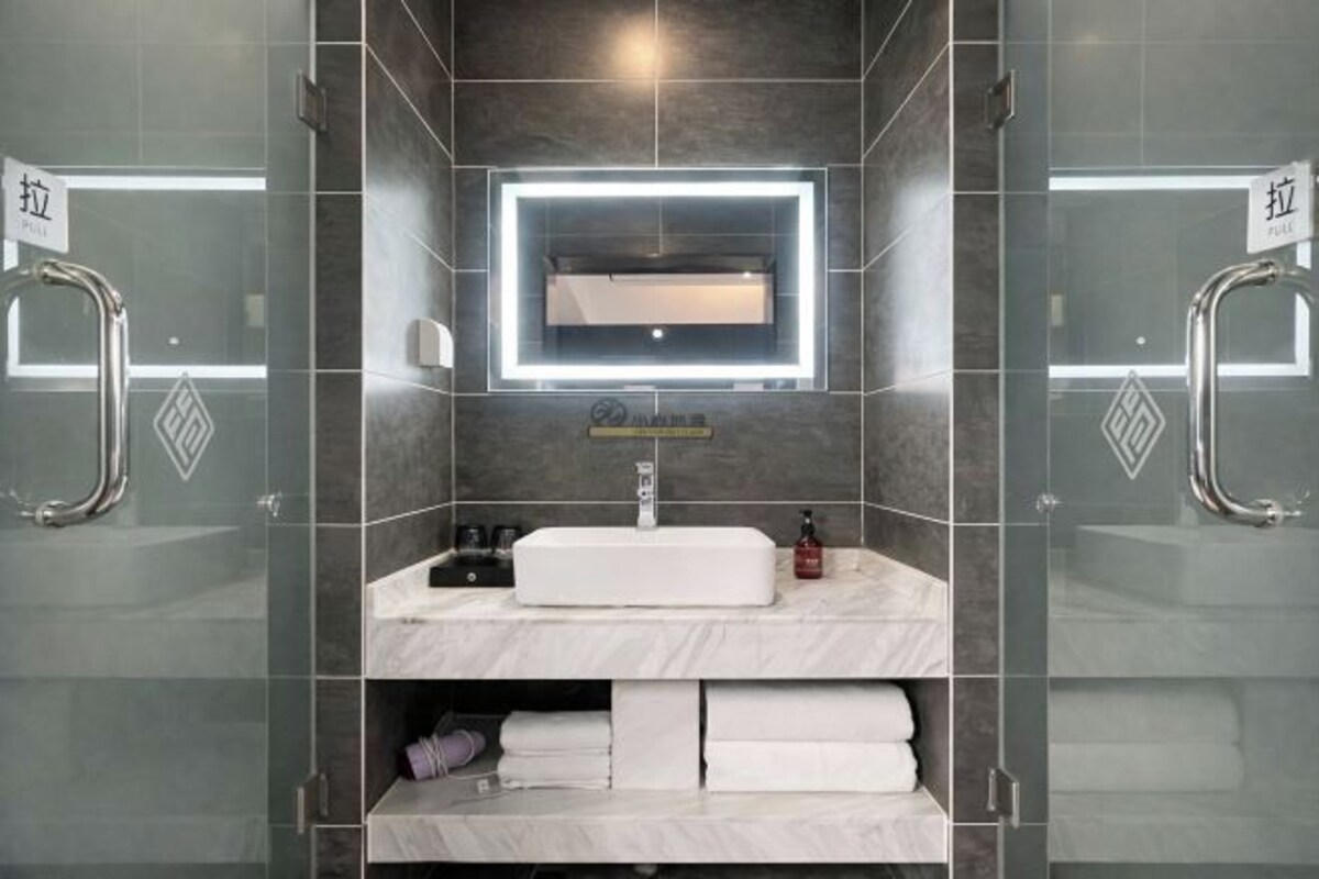 A modern bathroom with a glass partition, a built-in sink, a mirror with LED lighting, and a towel rack.