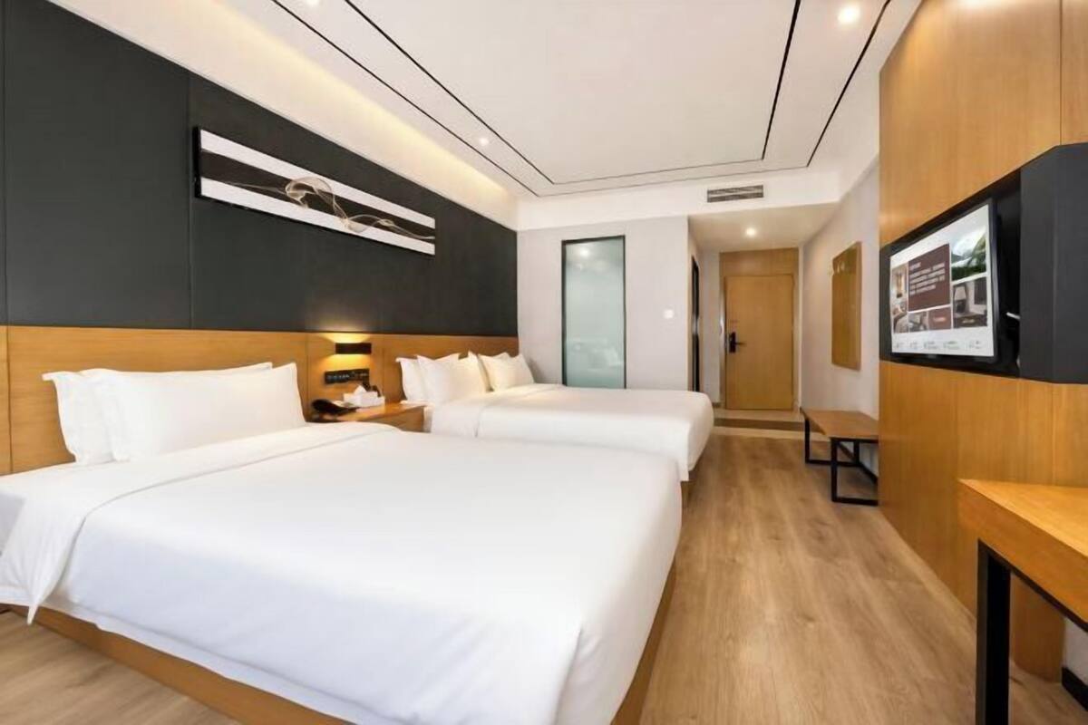 A hotel room with two beds, a TV, a wooden bench, and a wall-mounted artwork.