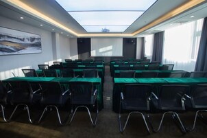 A conference room with a high ceiling, a projector screen, and rows of tables with chairs.