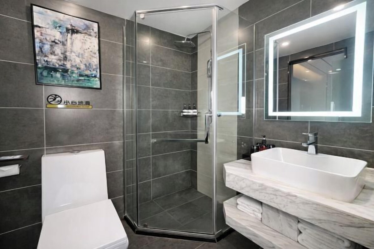 Un baño moderno con cabina de ducha de vidrio, inodoro blanco, espejo grande con iluminación integrada y encimera de mármol con lavabo.